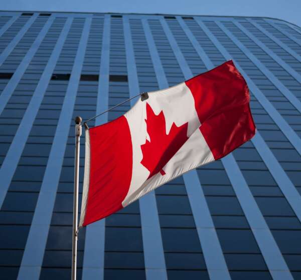 Canadian-flag-in-front-of-a-business-building-in-Ottawa-Ontario-Canada.-Ottawa-is-the-capital-city-of-Canada-and-one-of-the-main-economic-1-min